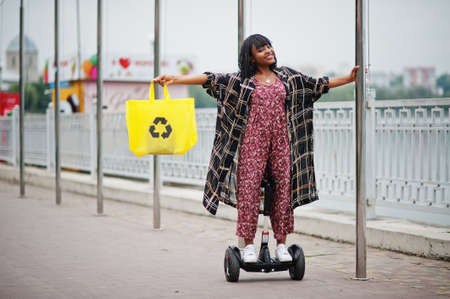 Beautiful african american woman using hoverboard. Black girl with yellow cloth eco bags recycling symbol.の写真素材