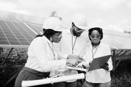 African american technician checks the maintenance of the solar panels. Group of three black engineers meeting at solar station.の写真素材
