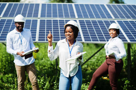 African american technician checks the maintenance of the solar panels. Group of three black engineers meeting at solar station.の写真素材