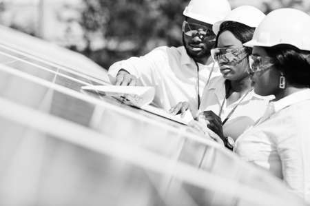 African american technician checks the maintenance of the solar panels. Group of three black engineers meeting at solar station.の写真素材