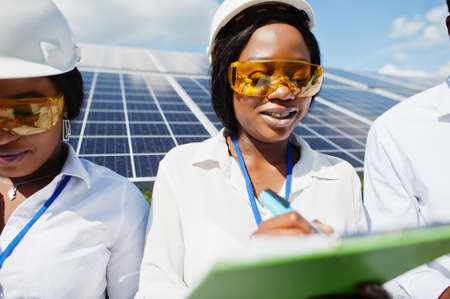African american technician checks the maintenance of the solar panels. Group of three black engineers meeting at solar station.の写真素材