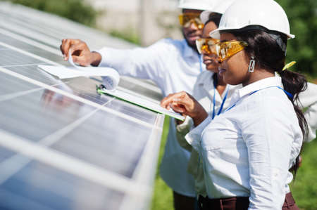 African american technician checks the maintenance of the solar panels. Group of three black engineers meeting at solar station.の写真素材