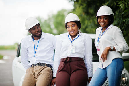 African american technician in white helmets near car. Group of three black engineers meeting.の写真素材