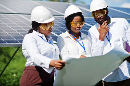 African american technician checks the maintenance of the solar panels. Group of three black engineers meeting at solar station.の写真素材