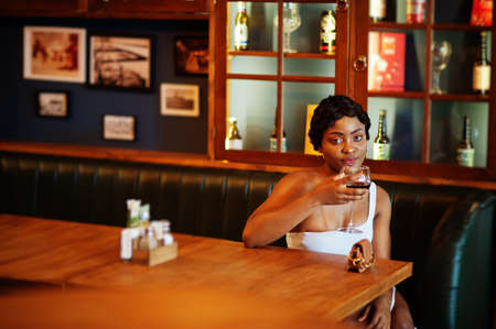 African american woman, retro hairstyle in white dress at restaurant with glass of wine.の写真素材