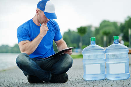 Delivery man sitting with clipboard water bottles outdoor.