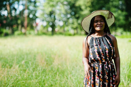 Portrait of gorgeous african american woman 20s in summer hat posing at green grass in park.の写真素材