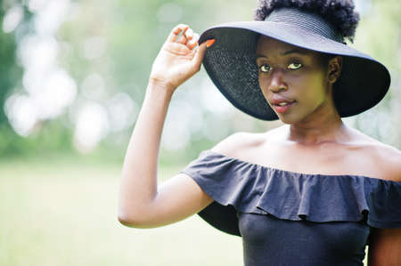 Portrait of gorgeous african american woman 20s in summer hat posing at green grass in park.の写真素材