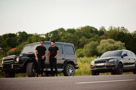 Two asian brothers man wear on all black posed near suv cars.