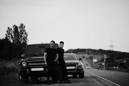 Two asian brothers man wear on all black posed near suv cars.