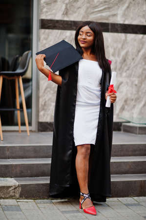 Young female african american student with diploma poses outdoors.
