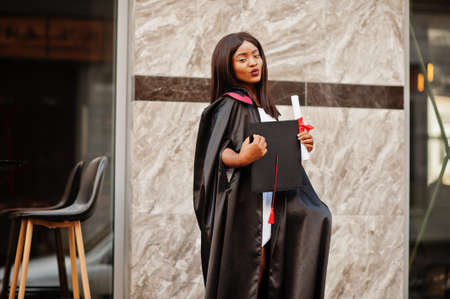 Young female african american student with diploma poses outdoors.