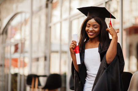 Young female african american student with diploma poses outdoors.