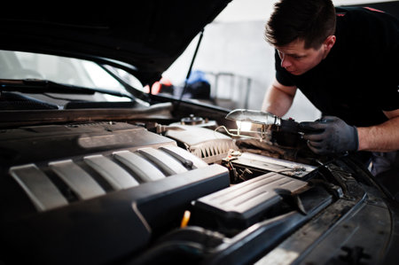 Car repair and maintenance theme. Mechanic in uniform working in auto service, checking engine.の写真素材