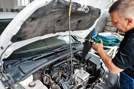 Car repair and maintenance theme. Mechanic in uniform working in auto service, pouring new motor oil.の写真素材