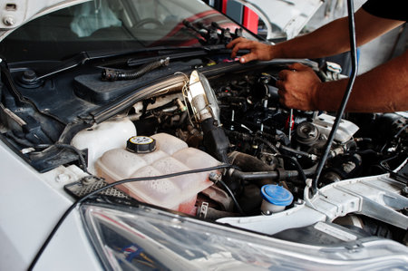 Car repair and maintenance theme. Mechanic in uniform working in auto service, checking engine.の写真素材