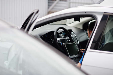 Car repair and maintenance theme. Electric mechanic in uniform working in auto service, making car diagnostics using obd device with laptop.の写真素材