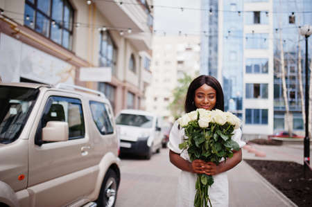Beautiful african american girl holding bouquet of white roses flowers on dating in the city. Black...