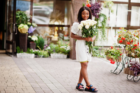 Beautiful african american girl holding bouquet of white roses flowers on dating in the city. Black businesswoman with bunch of flowers.の写真素材