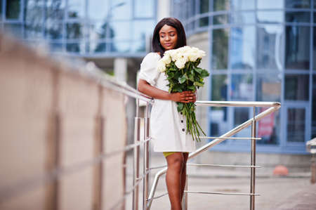 Beautiful african american girl holding bouquet of white roses flowers on dating in the city. Black businesswoman with bunch of flowers.の写真素材