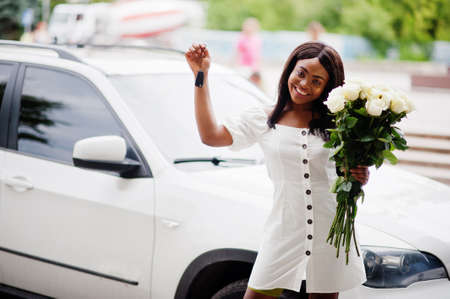 Beautiful african american girl holding bouquet of white roses flowers on dating in the city. Black businesswoman with bunch of flowers hold keys of her new present car.の写真素材