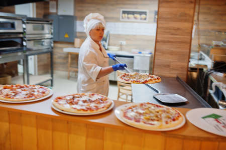 Female chef preparing pizza in restaurant kitchen.