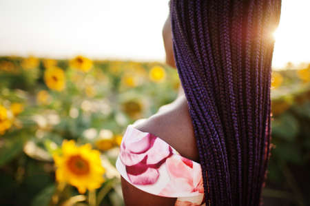 Pretty young black woman wear summer dress pose in a sunflower field.