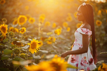 Pretty young black woman wear summer dress pose in a sunflower field.の写真素材