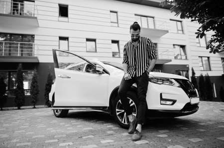 Successful arab man wear in striped shirt and sunglasses pose near his white suv car. Stylish...