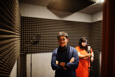 Young asian duet singers with microphone recording song in record music studio.