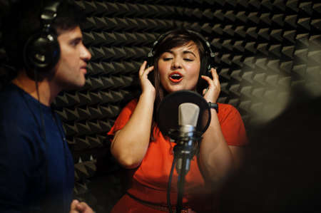 Young asian duet singers with microphone recording song in record music studio.
