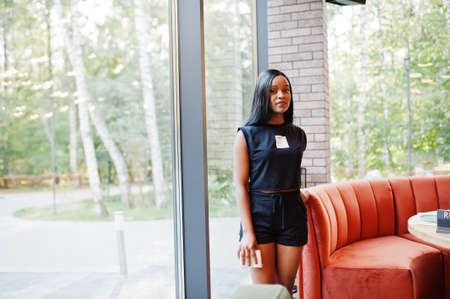 Fashionable feminist african american woman wear in black t-shirt and shorts, posed at restaurant.