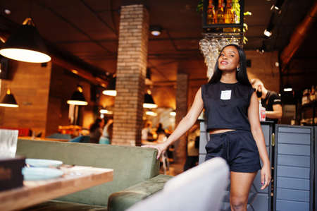 Fashionable feminist african american woman wear in black t-shirt and shorts, posed at restaurant.