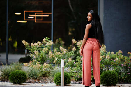 Fashionable african american woman in peach pants and black blouse pose outdoor.の写真素材