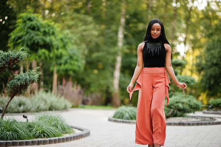 Fashionable african american woman in peach pants and black blouse pose outdoor.の写真素材