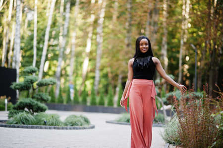 Fashionable african american woman in peach pants and black blouse pose outdoor.の写真素材