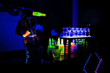 Professional barman and led light show. Silhouette of modern bartender shaking drink at night...