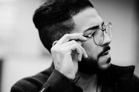 Close up portrait of middle eastern beard entrepreneur wear black coat and blue shirt, eyeglasses against office building.の写真素材