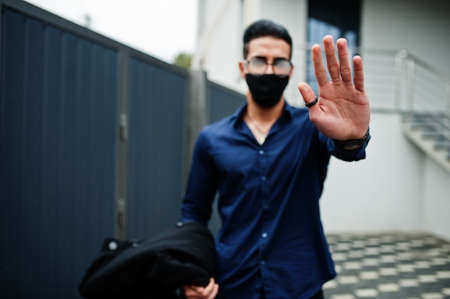 Middle eastern entrepreneur wear black face mask and eyeglasses show stop sign by hand. New normal...