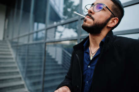 Middle eastern entrepreneur wear black coat and blue shirt, eyeglasses against office building...