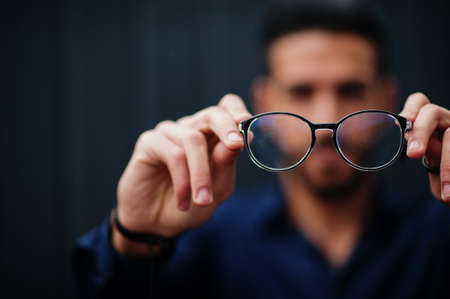 Middle eastern entrepreneur wear blue shirt show close up eyeglasses, against steel wall.
