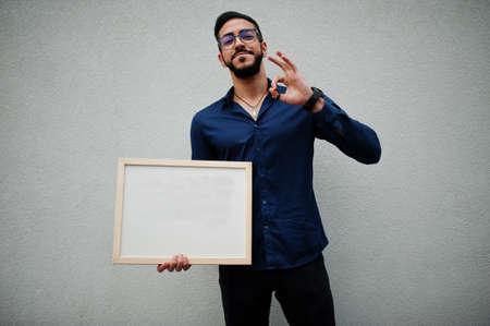 Middle eastern man wear blue shirt, eyeglasses, hold white empty board.