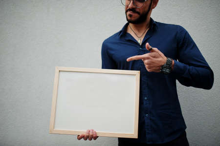 Middle eastern man wear blue shirt, eyeglasses, hold white empty board.の写真素材
