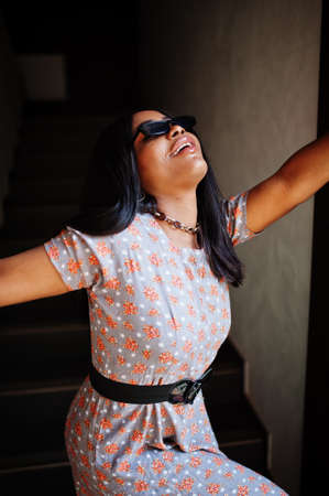 Fashion portrait of african american woman in long dress and eyeglasses indoor.