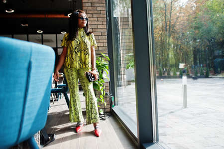 Glamor african american woman wear fashionable snake dress and sunglasses pose at restaurant.