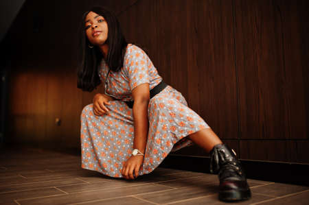Fashion portrait of african american woman in long dress, boots indoor.