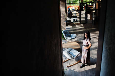 Fashion portrait of african american woman in long dress, boots and sunglasses indoor.