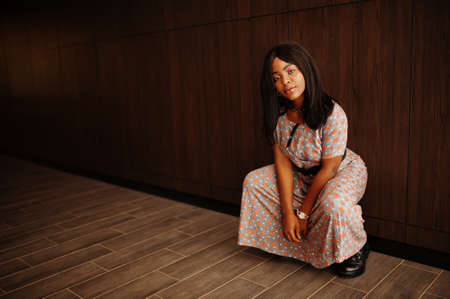 Fashion portrait of african american woman in long dress, boots indoor.