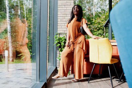 Portrait of beauty young black woman, wear orange outfit, pose at restaurant.