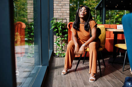 Portrait of beauty young black woman, wear orange outfit, pose at restaurant.の写真素材